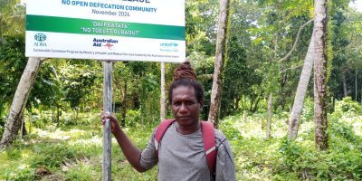 Chris-Panakera-taking-photo-Infront-of-signboard-at-his-community-in-Rannogah.jpg